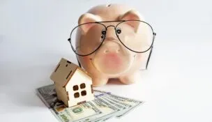 Piggybank with wooden house and dollars. Isolated on white background
